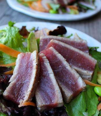 Close up of sliced rare ahi tuna steaks over salad.