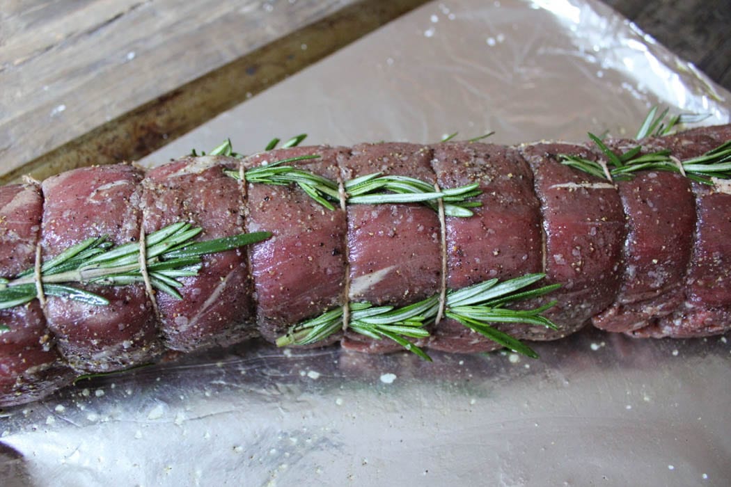 Beef tenderloin that's oiled and seasoned with rosemary sprigs threaded through kitchen twine.