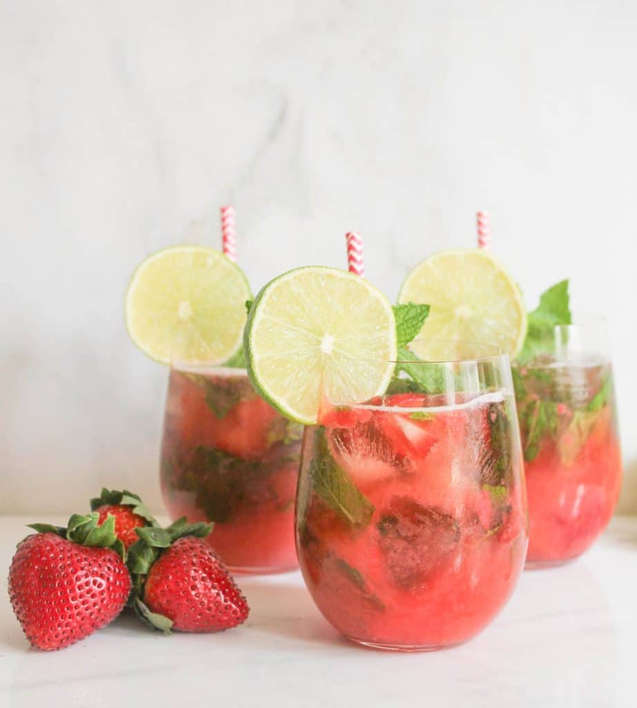 Three glasses of Roasted Strawberry Mojito garnished with limes slices and mint.