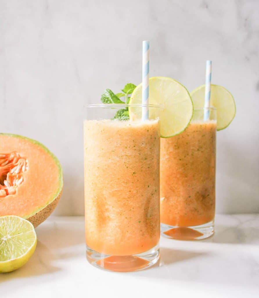 Two glasses of Cantaloupe Coolers garnished with slices of lime.