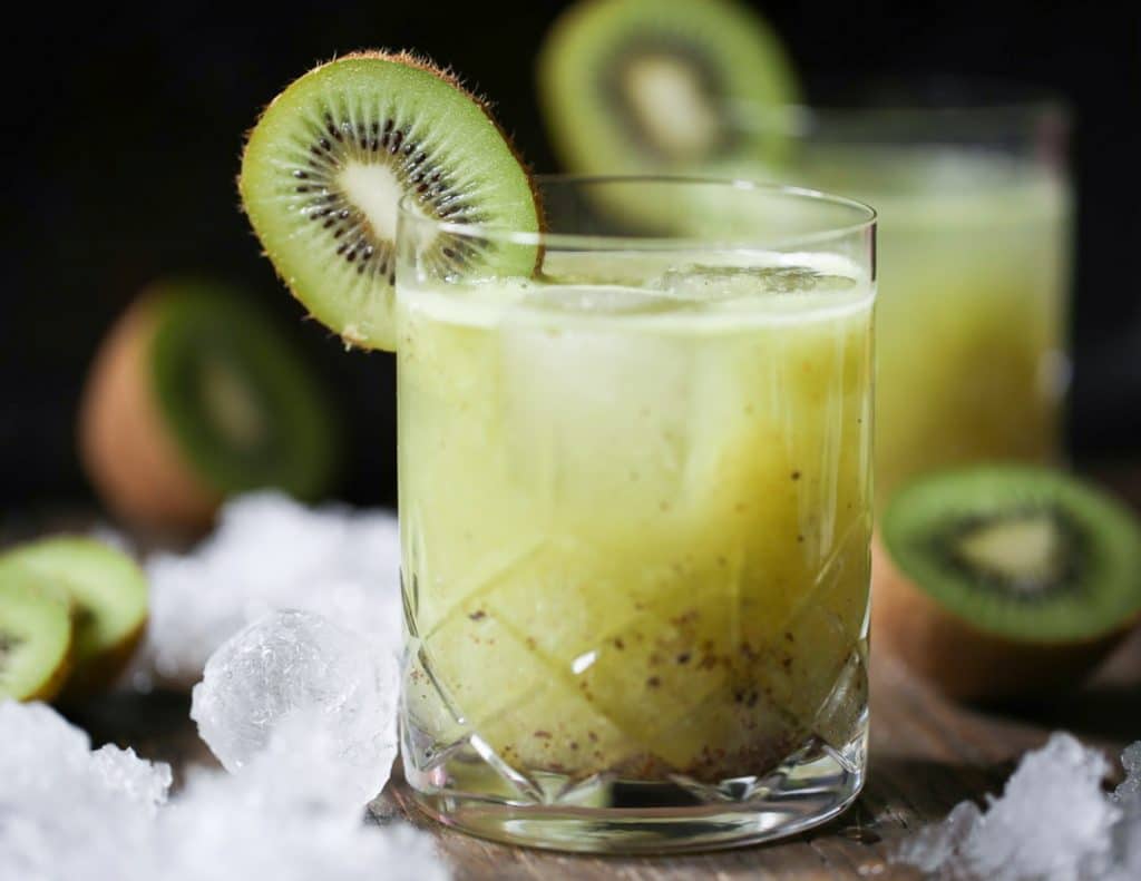 Two glasses of Kiwi Kiss Cocktail garnished with a slice of kiwi.