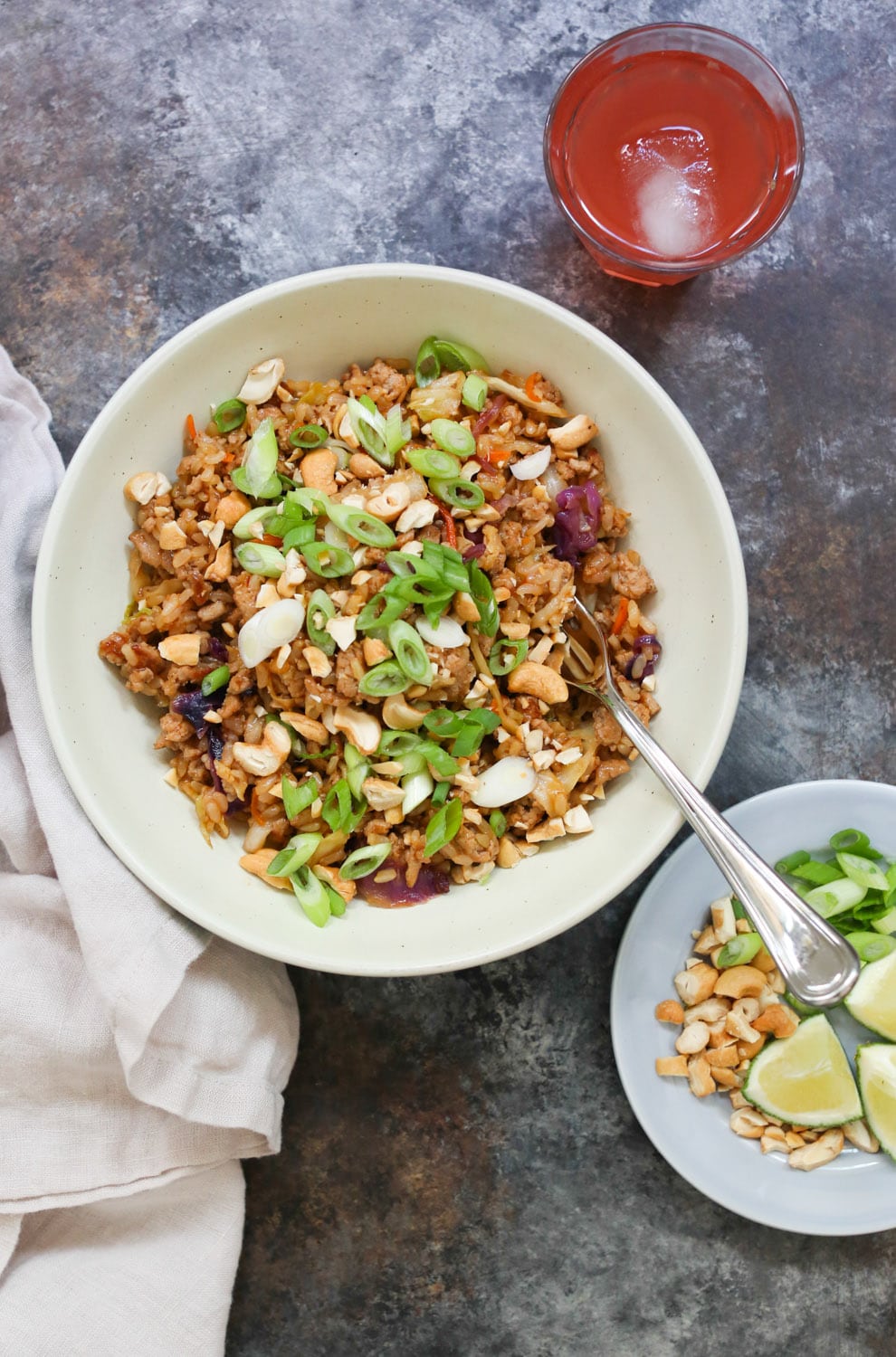Overhead view of one stir-fried turkey and rice bowl with a small side plate of topping peeking in from the lower right corner.