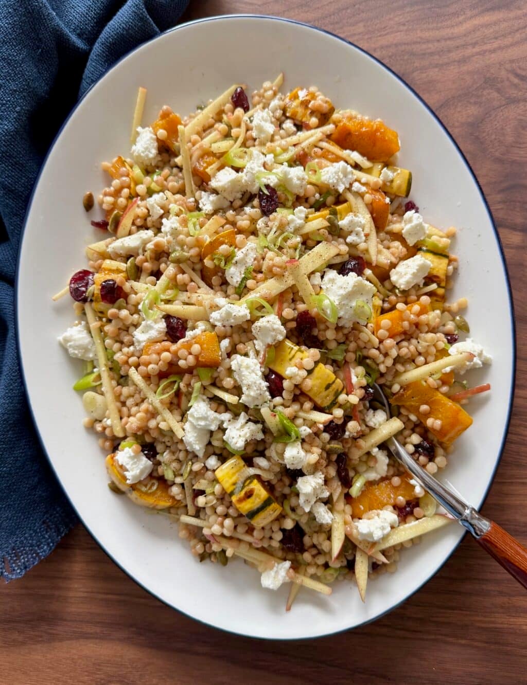 Overhead shot of fall couscous salad on a platter with a serving spoon and napkin.